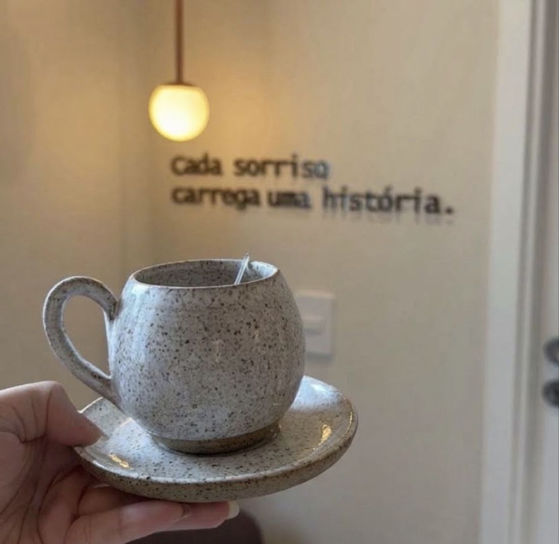 Xícara de café em frente à parede com a frase Cada sorriso carrega uma história